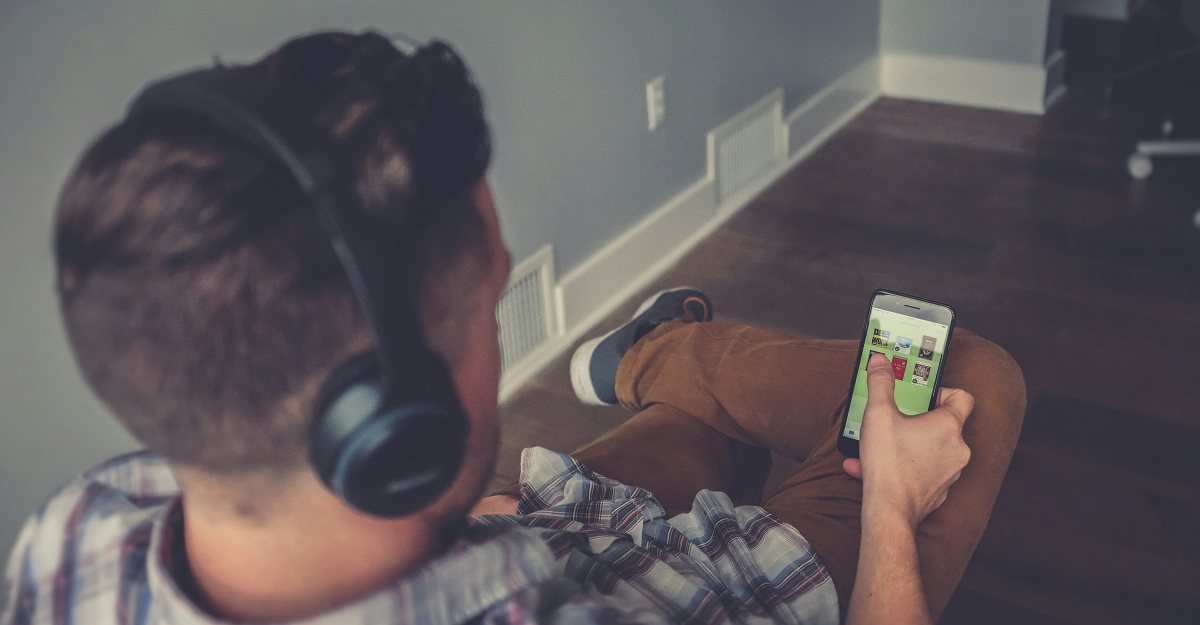 Homem usando headphones para ouvir um audiobook em seu smartphone.